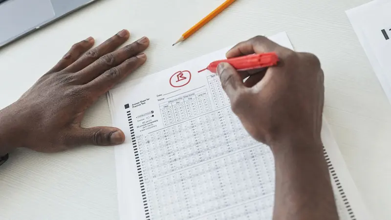 Mano corrige con plumón rojo una hoja de respuestas de un examen en papel